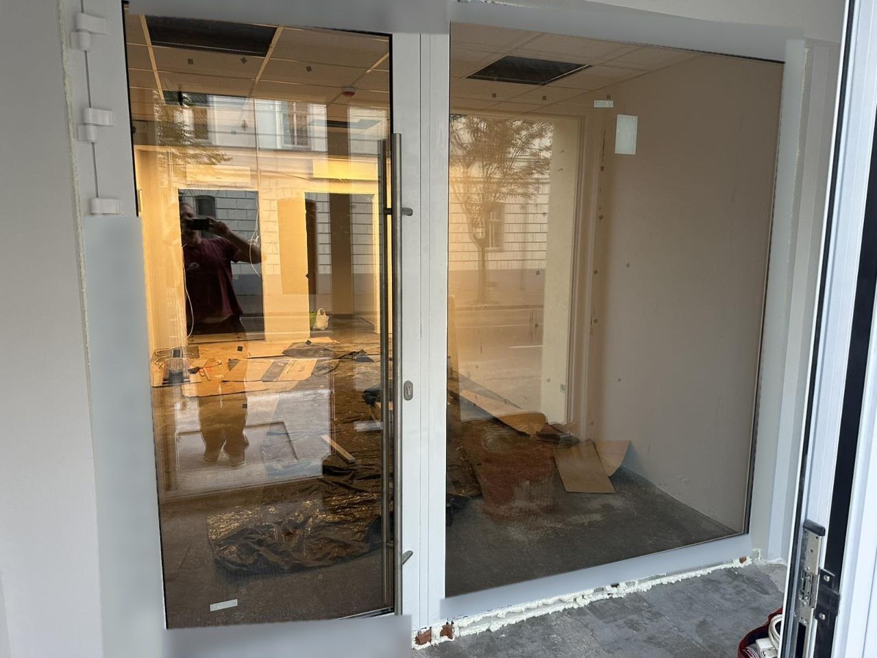 Puerta doble de aluminio blanca con tirador largo junto a un gran fijo, recién instalada en un local