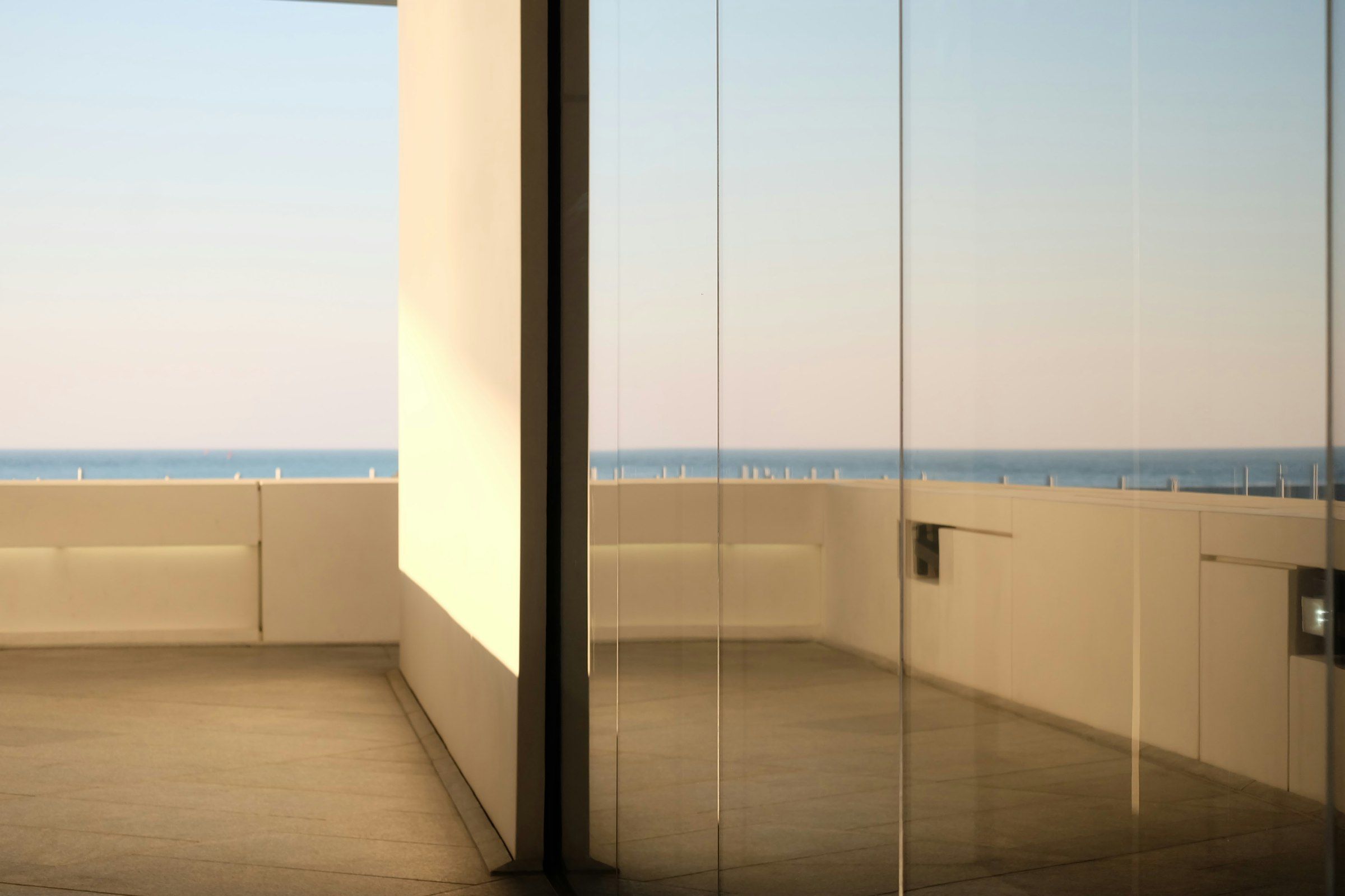 Floor-to-ceiling frameless glass panels with the sea on the horizon