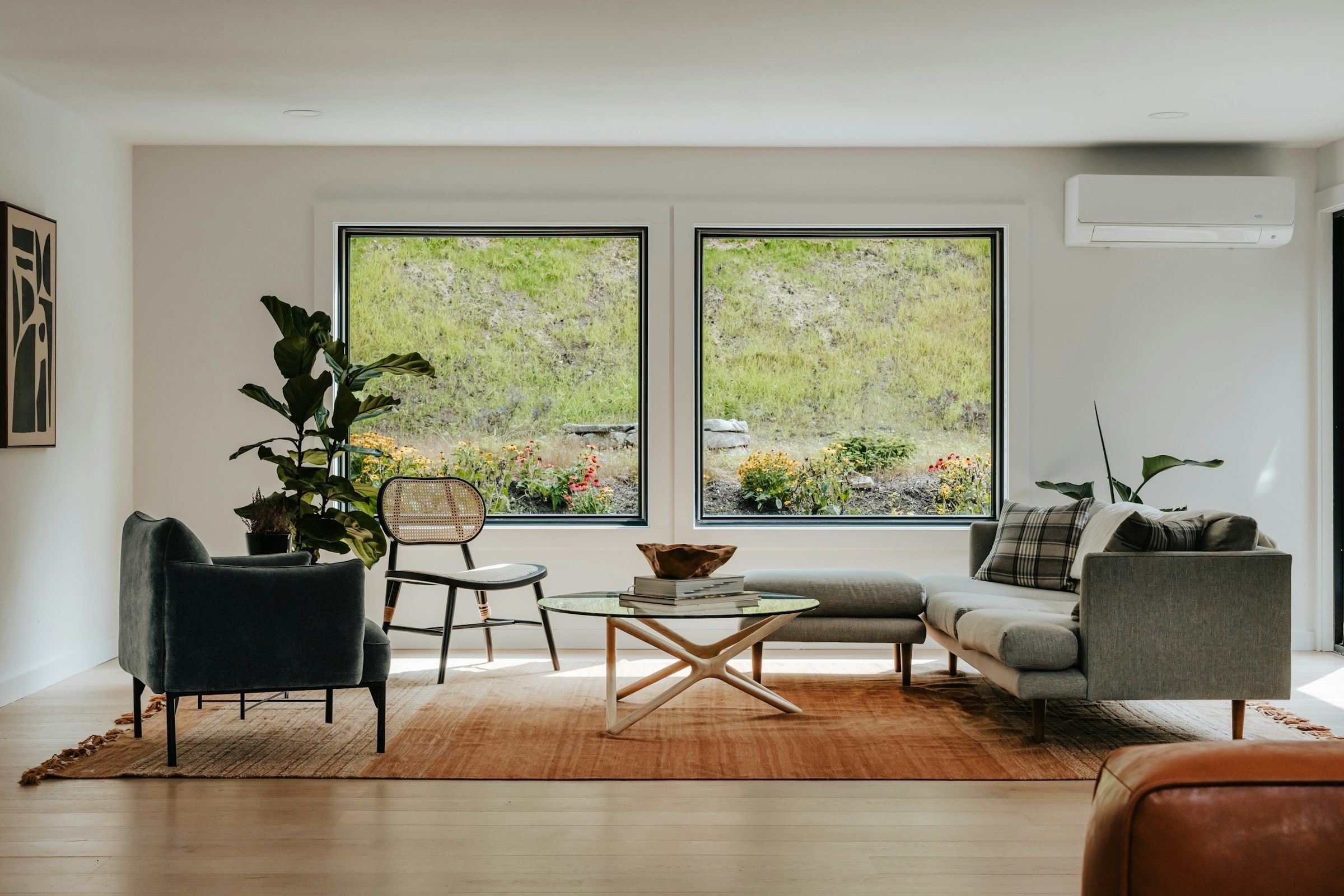 Salón luminoso con dos grandes ventanas de marco antracita que dan a una ladera verde