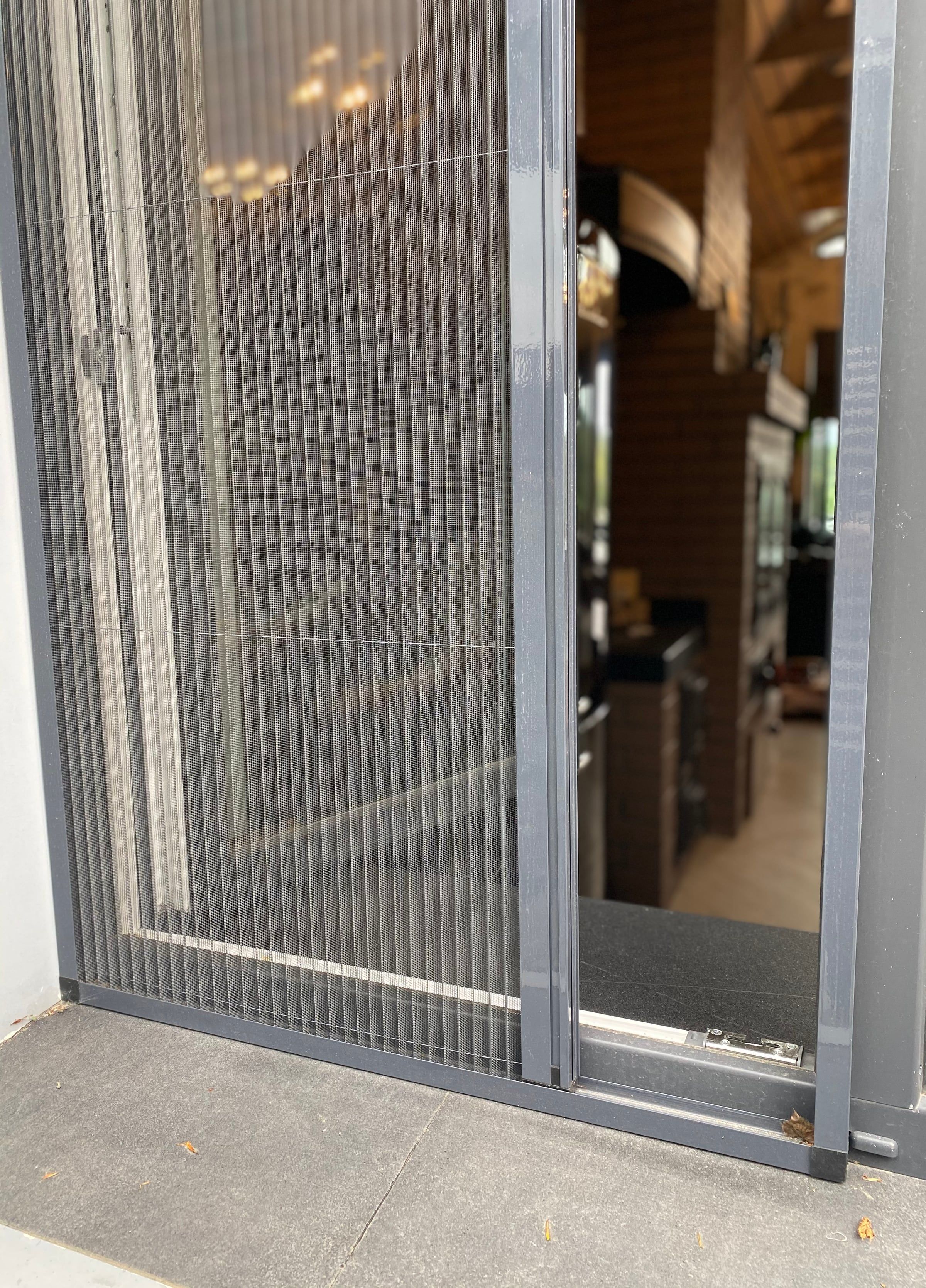 Mosquitera plisada medio cerrada en una puerta de balcón antracita