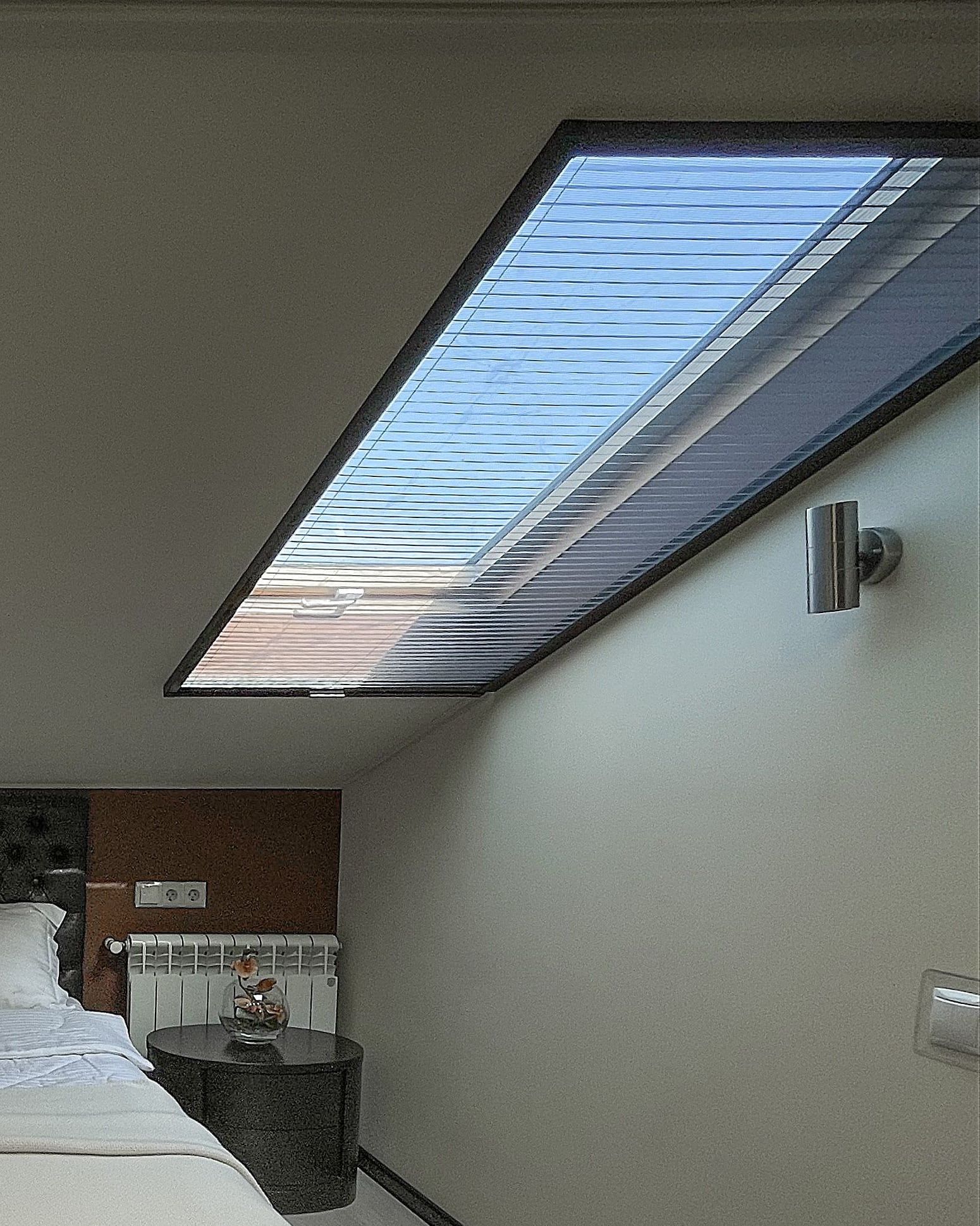 Sloped roof window in an attic bedroom with a plissé fly screen drawn across it