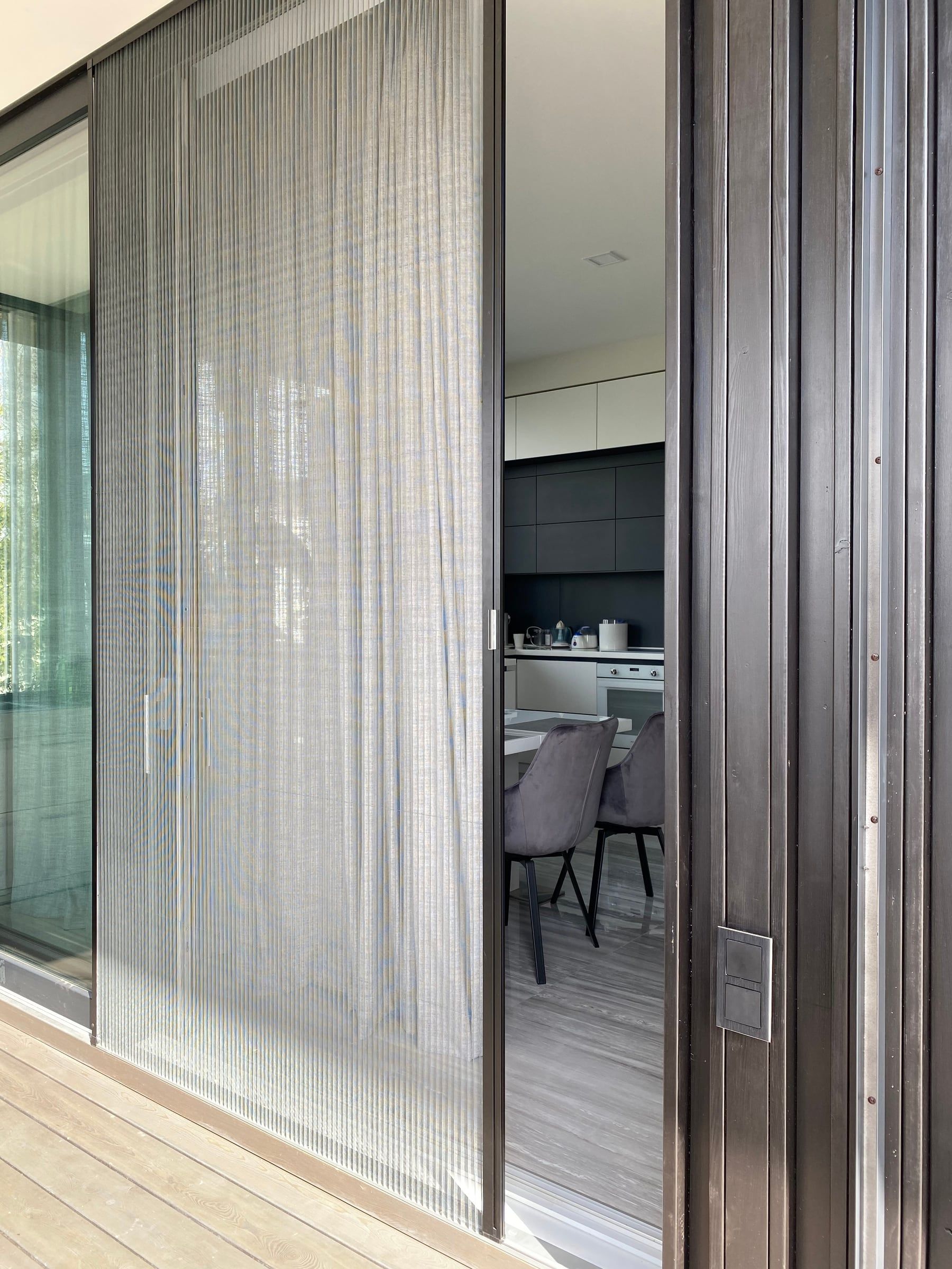 Plissé fly screen drawn across a dark sliding door, with a kitchen and dining area behind