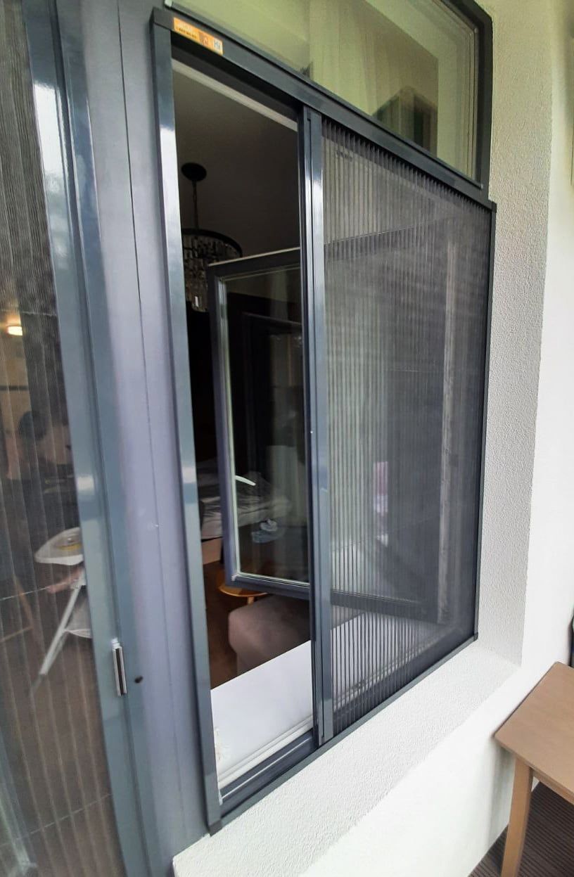 Window with the sash opened inwards and a plissé fly screen drawn across the opening