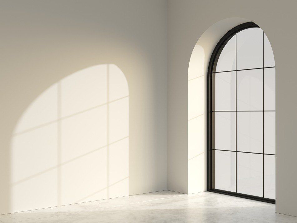 Tall dark-framed arched window with glazing bars in a bright empty room