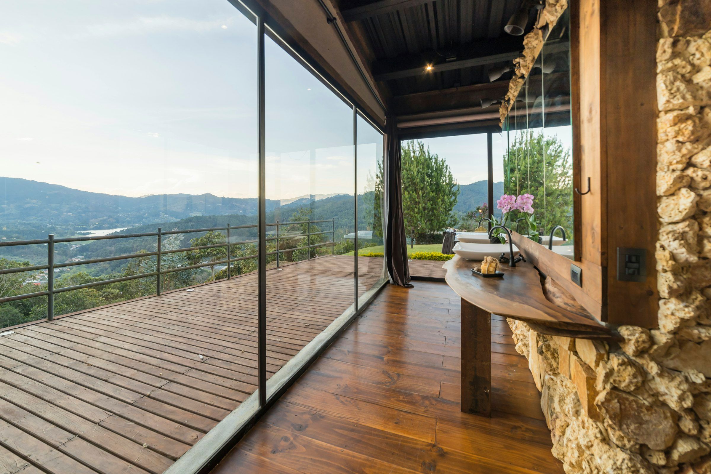 Terraza de madera cerrada con paneles de cristal sin perfiles, con vistas a colinas verdes